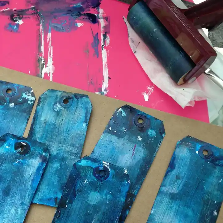 Rouleau chargé d’encre bleue posé sur une feuille rose, étiquettes encrées à côté