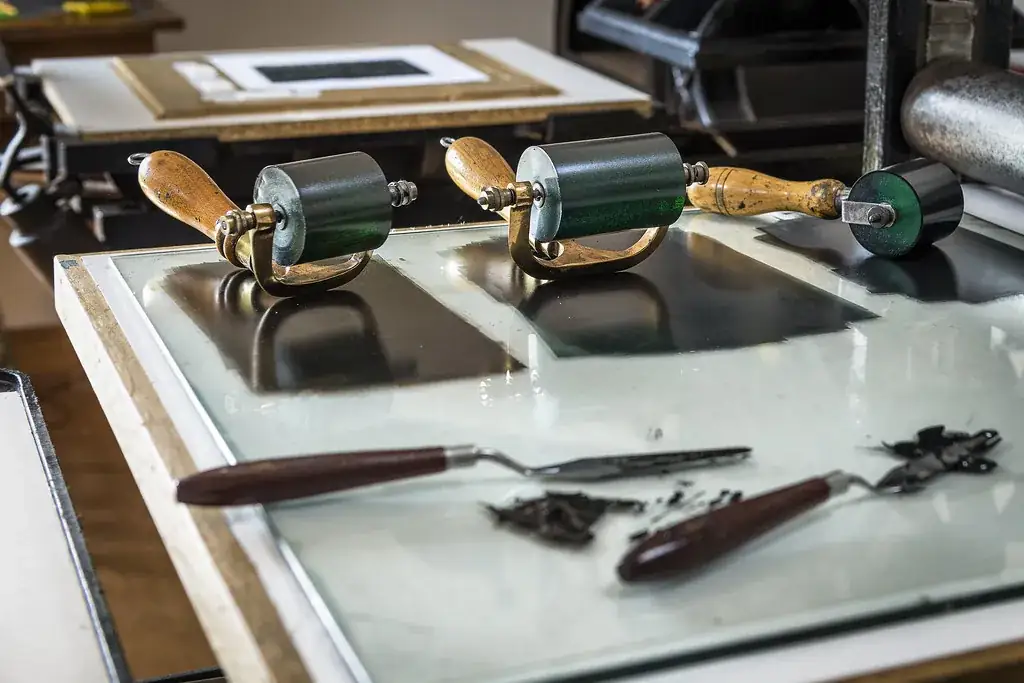 Deux rouleaux encreurs et des racles à encre posés sur une plaque de verre, dans l’atelier